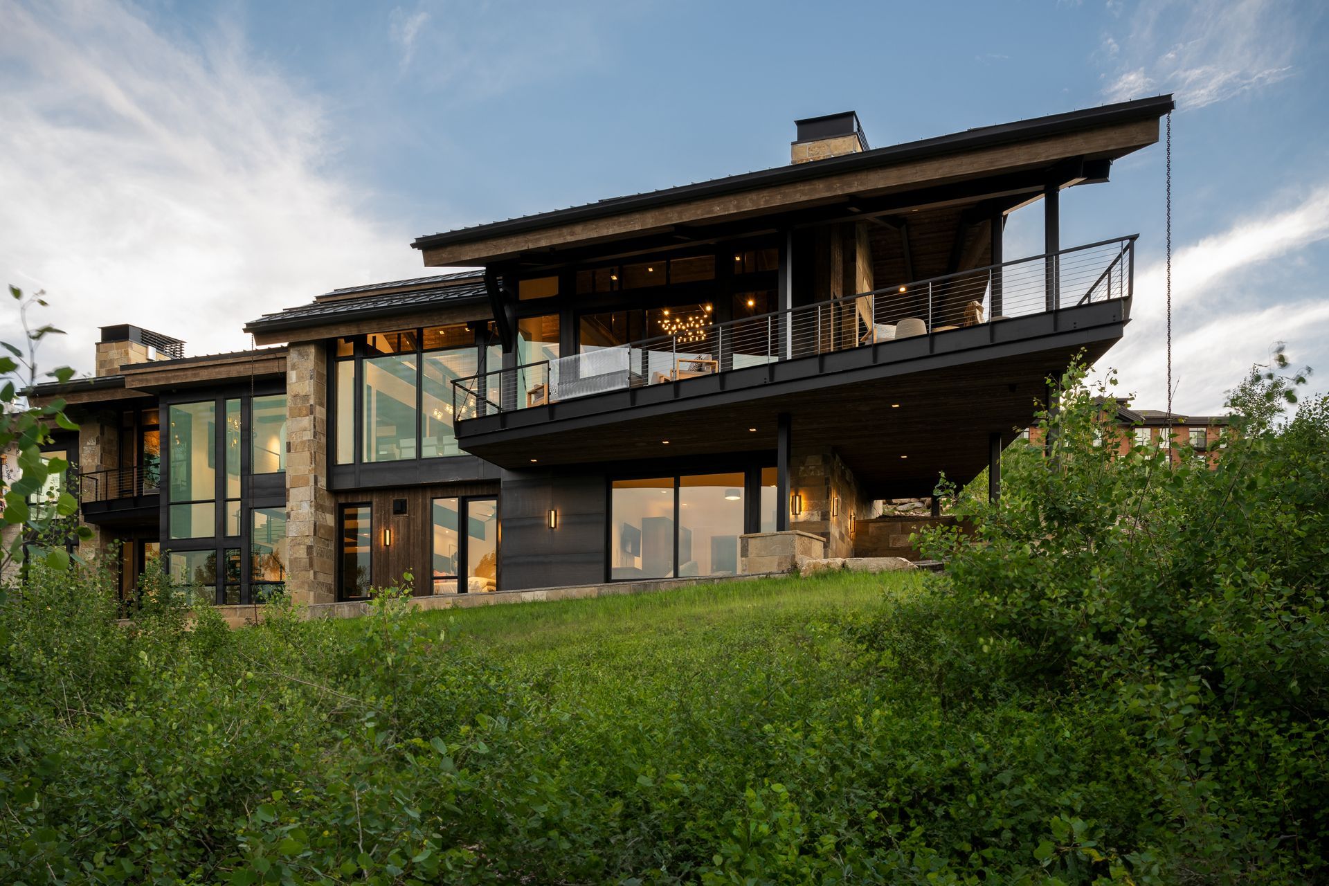 A large modern house is sitting on top of a grassy hill surrounded by trees.