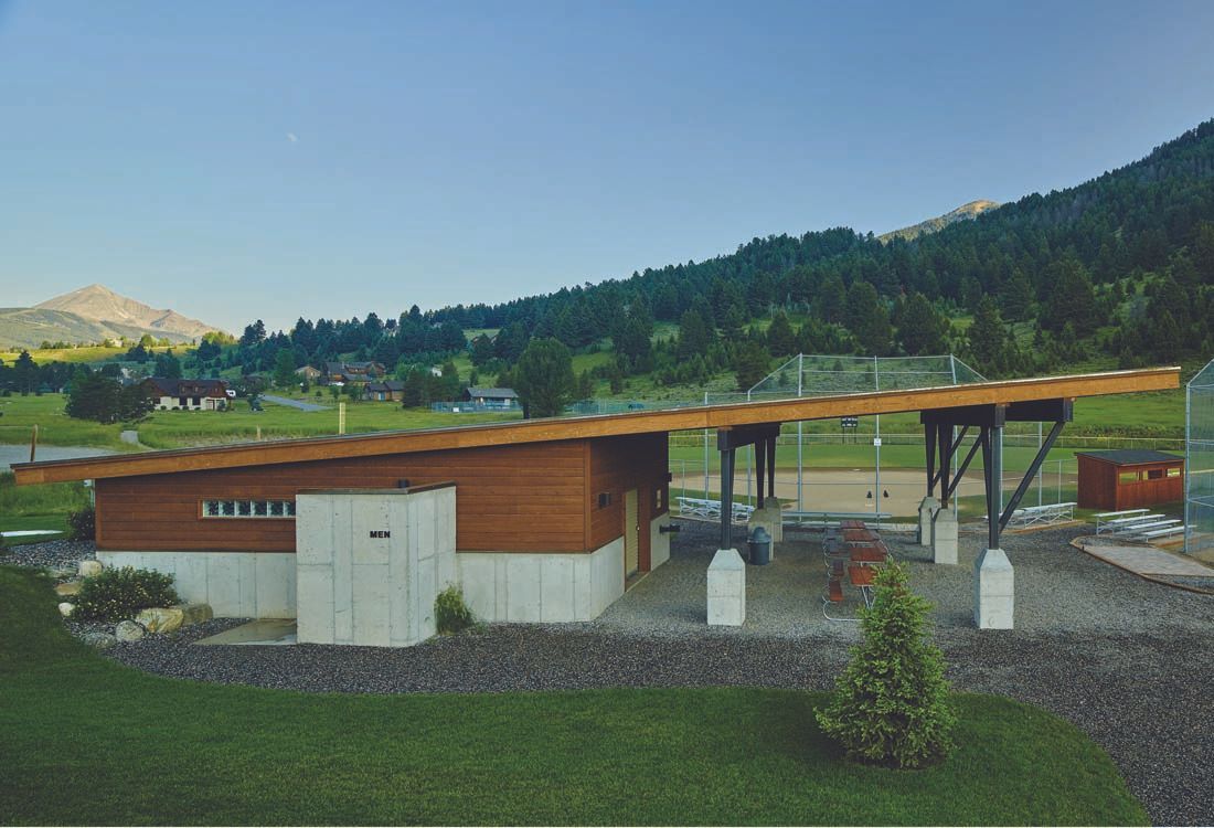 A wooden house with a roof that is covered in solar panels is sitting in the middle of a grassy field.