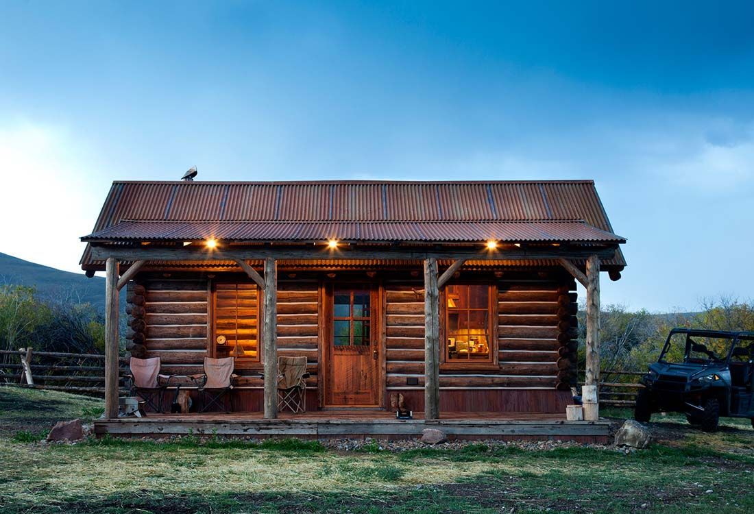 A small log cabin with a porch and a jeep parked in front of it.
