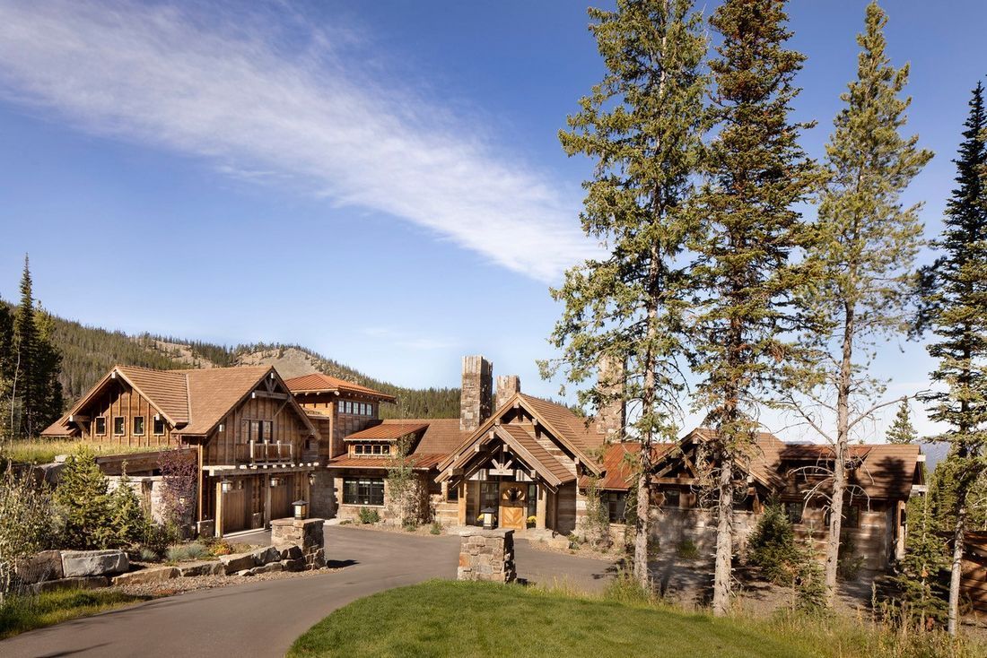A large house is surrounded by trees and mountains on a sunny day.