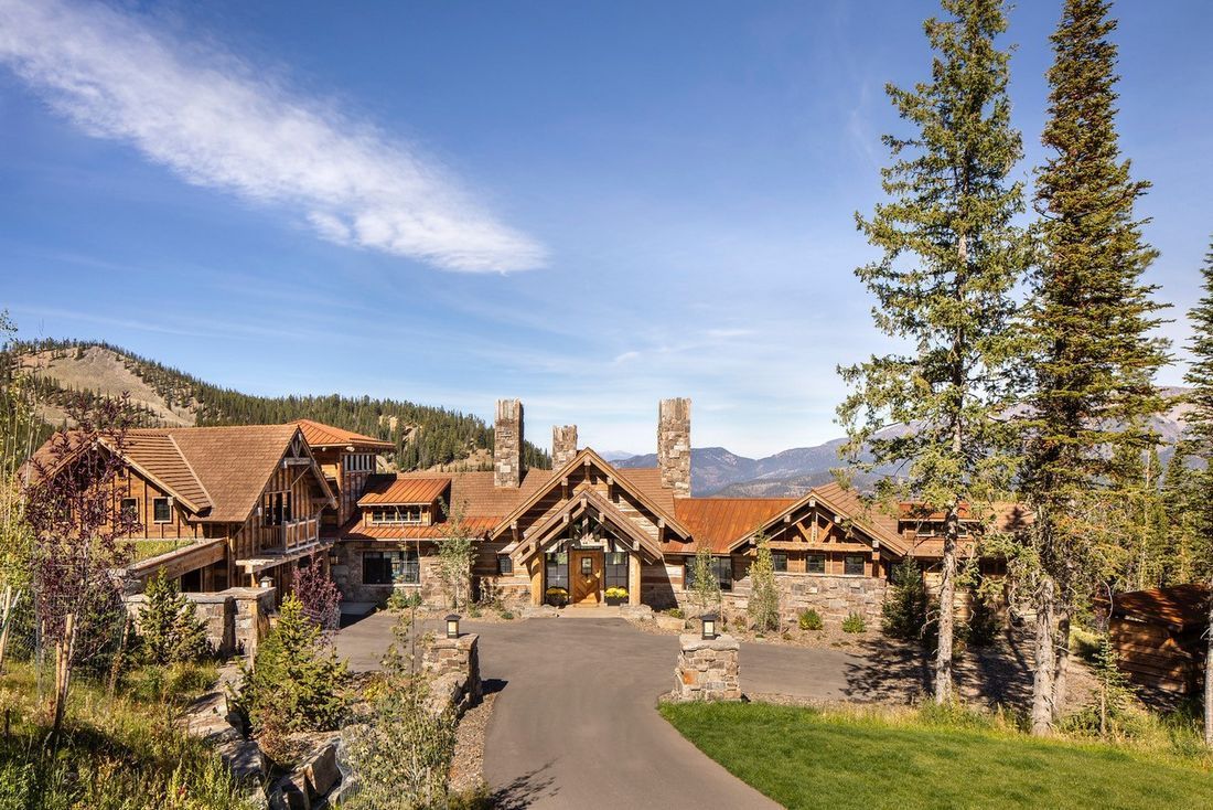 A large house with a driveway leading to it is surrounded by trees and mountains.