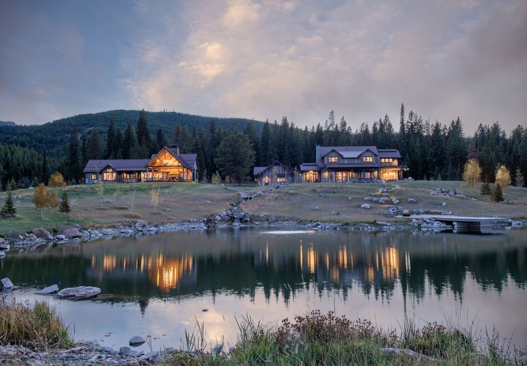A large house is sitting on top of a hill next to a lake surrounded by trees.
