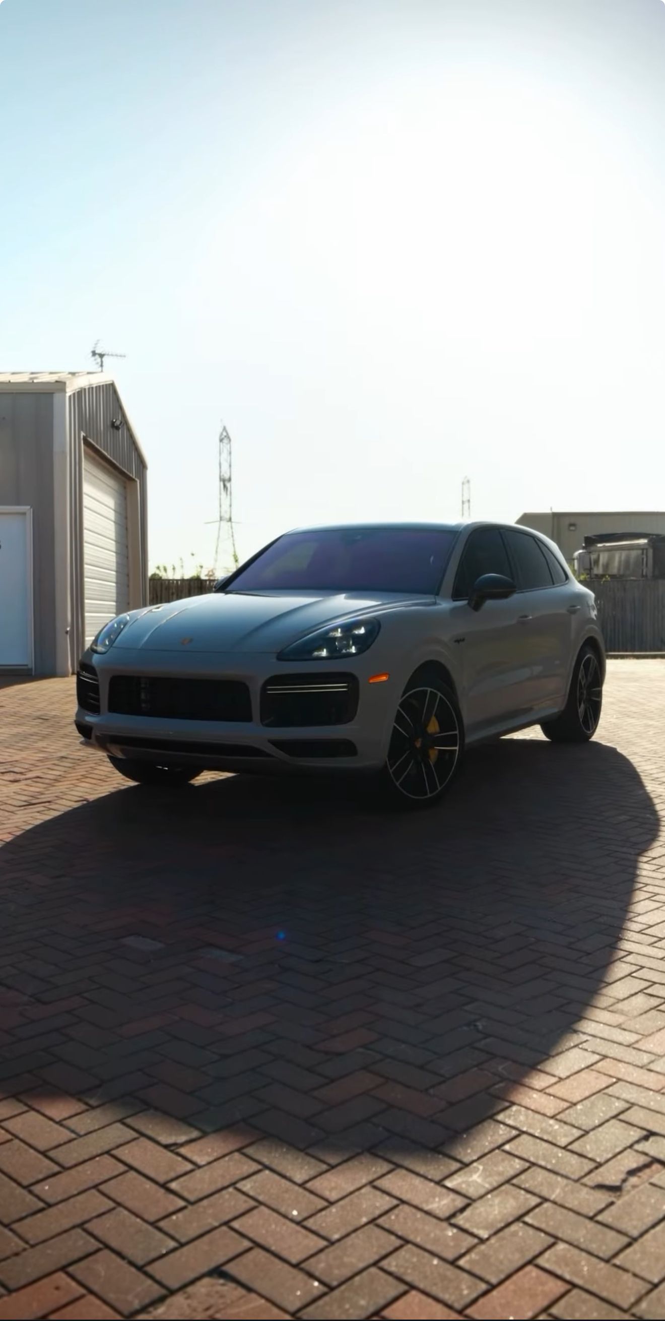 Gray Porsche SUV parked on a brick surface, casting a long shadow under the bright sun.
