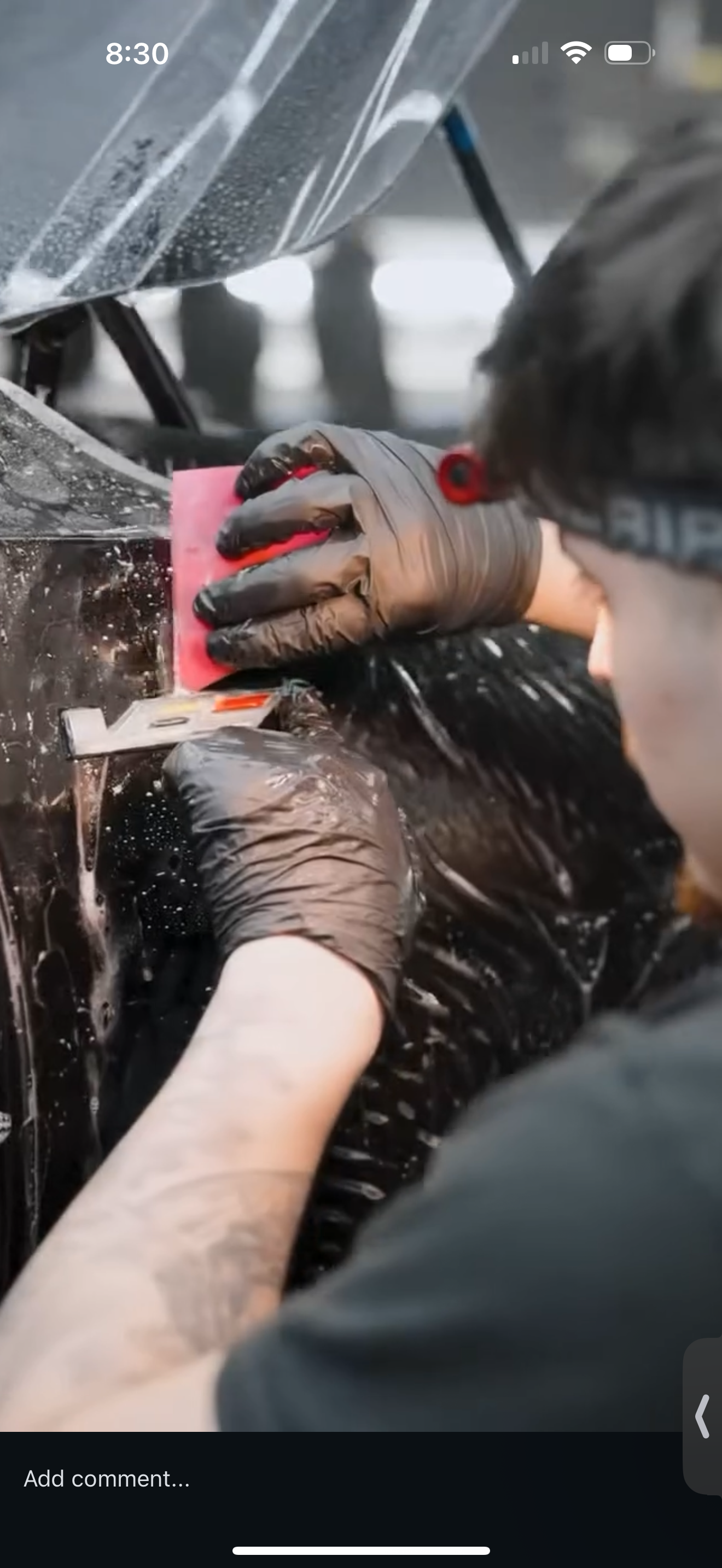 Person wearing black gloves applying tint to a car window with a red tool.