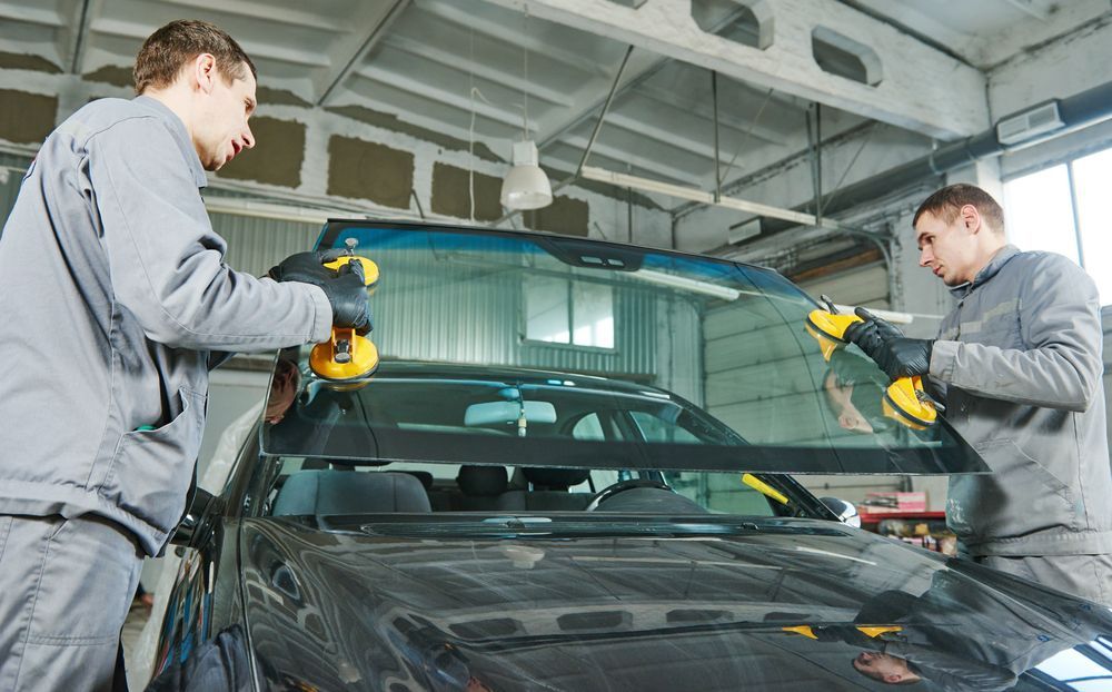 Two Men Are Installing A Windshield On A Car In A Garage — Eurobodalla Windscreens in Moruya, NSW
