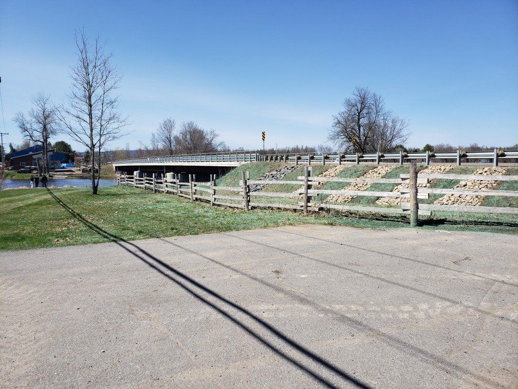 Une clôture en bois le long d'une route avec un pont en arrière-plan.