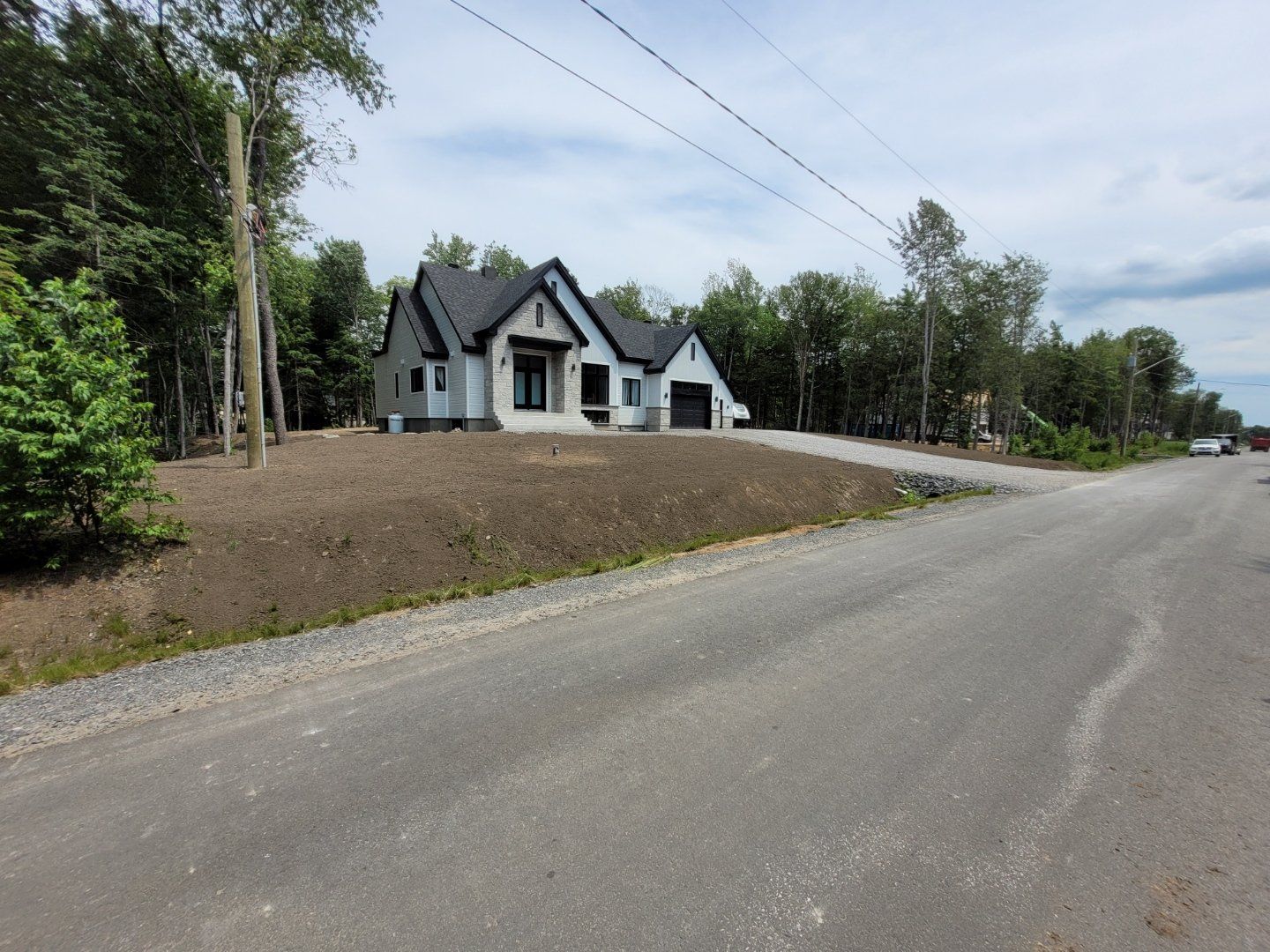 Une maison blanche avec un toit noir est sur le bord d'une route