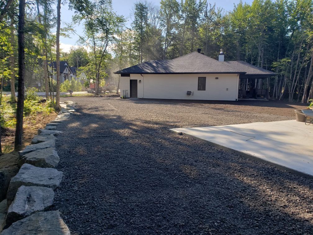 Une maison est située au milieu d'une allée de gravier entourée d'arbres.