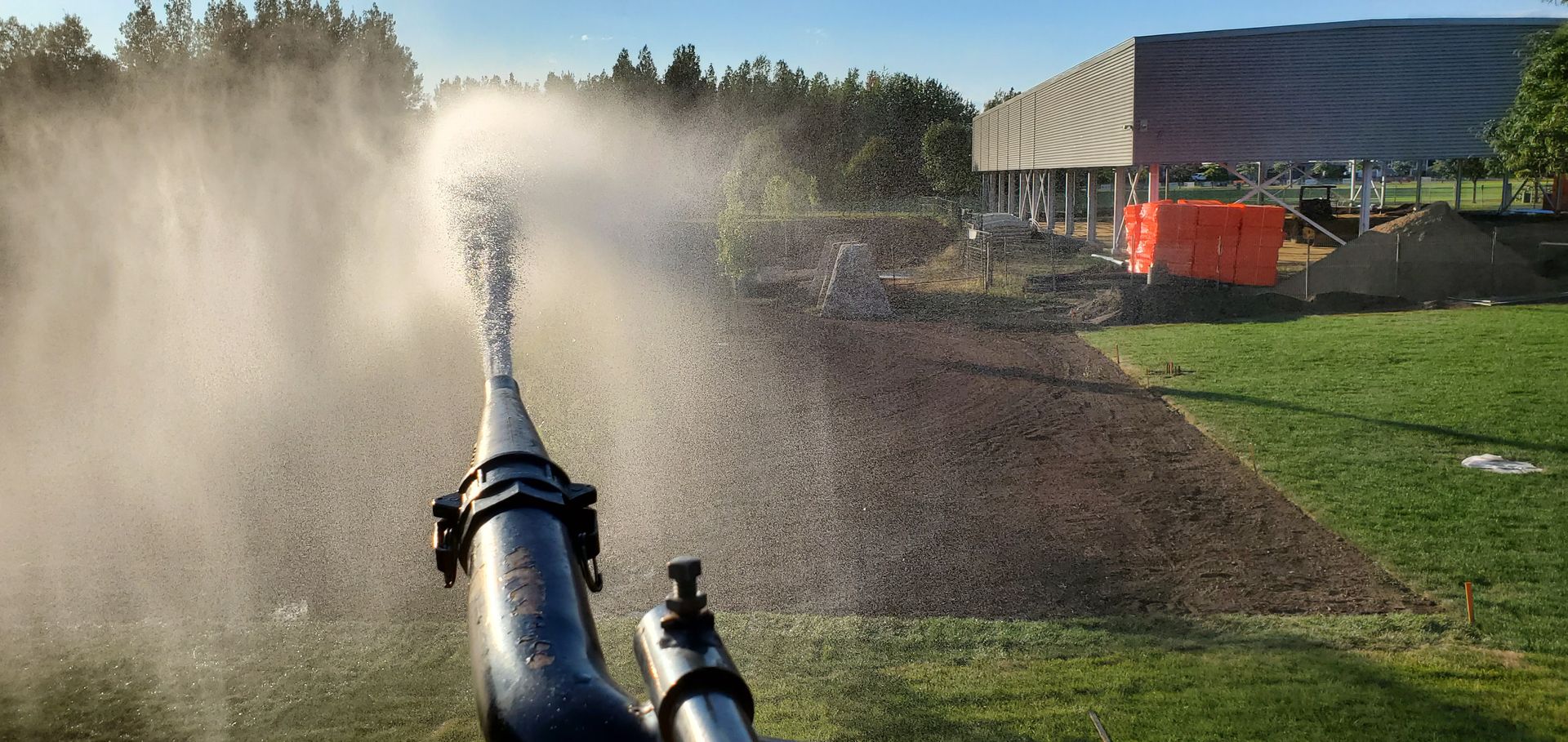 Un tuyau pulvérise de l'eau sur un champ herbeux.