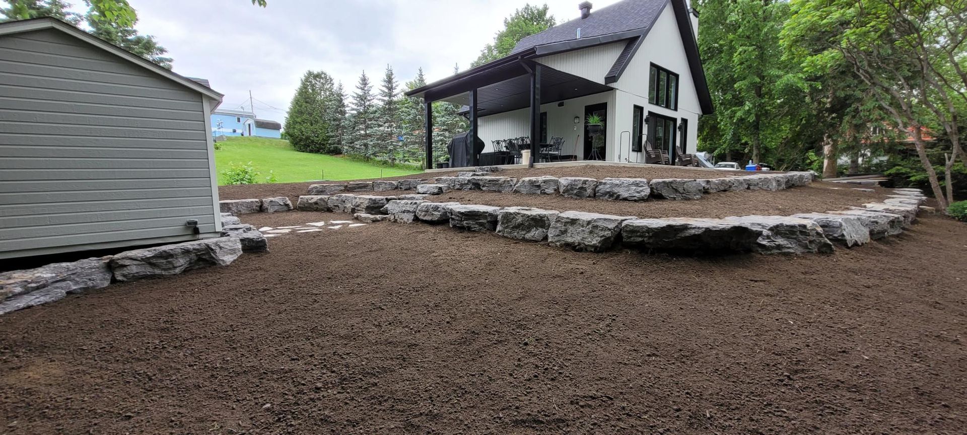 Une maison blanche est assise au sommet d'une colline de terre à côté d'un hangar.