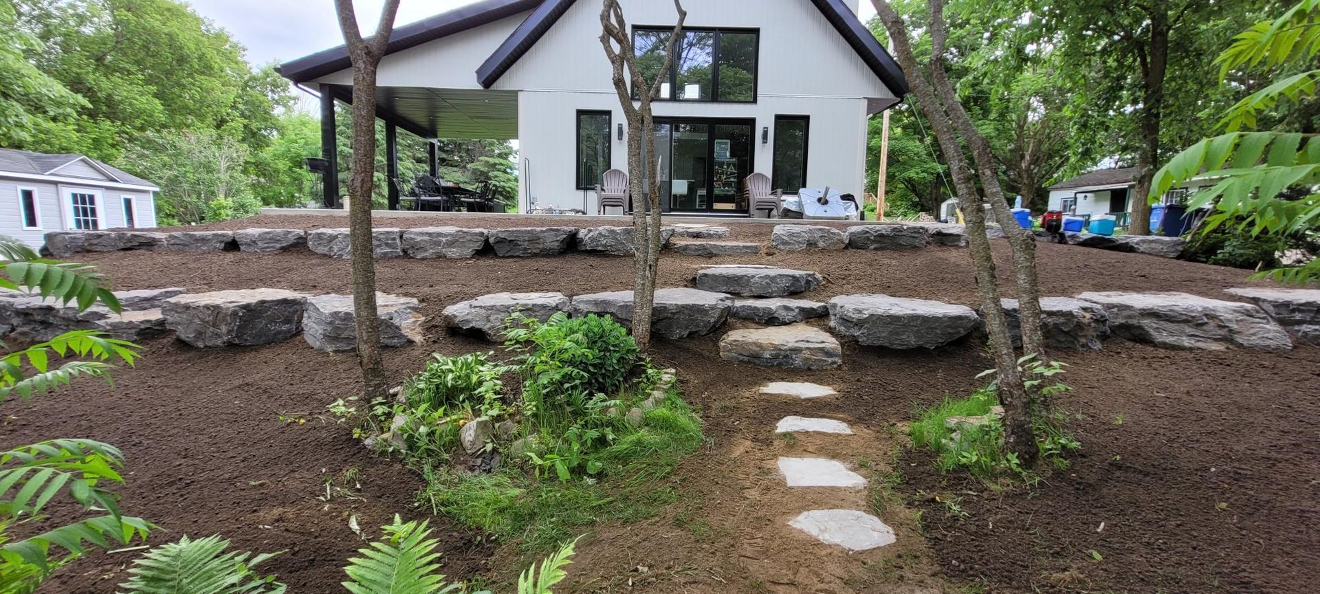 Une maison blanche avec une passerelle qui y mène est entourée d'arbres et de rochers.
