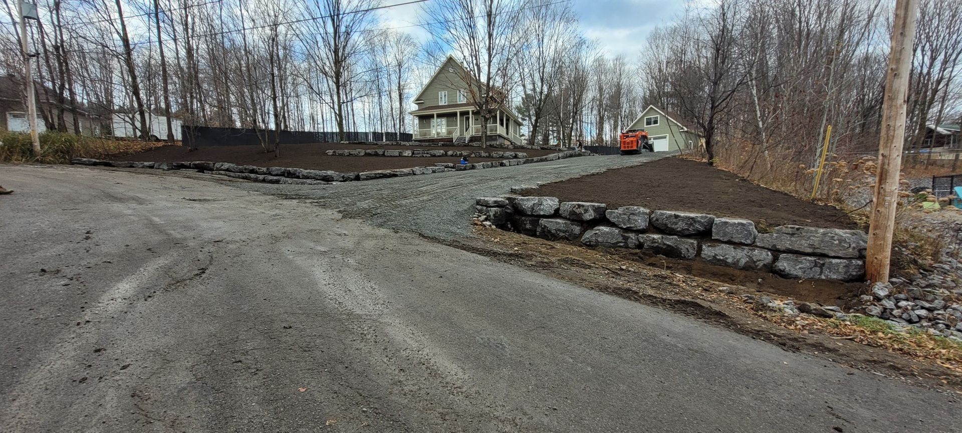 Un chemin de terre avec un mur de pierre sur le côté et une maison en arrière-plan.