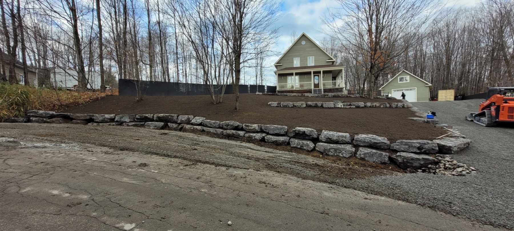 Une maison est en construction dans les bois à côté d'une allée de gravier.