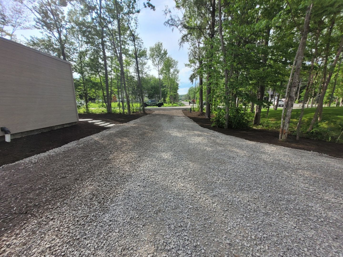 Une allée de gravier menant à une maison entourée d'arbres.