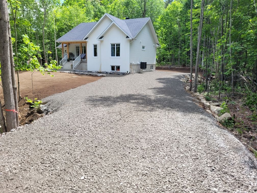 Une maison blanche avec une allée de gravier devant elle entourée d'arbres.