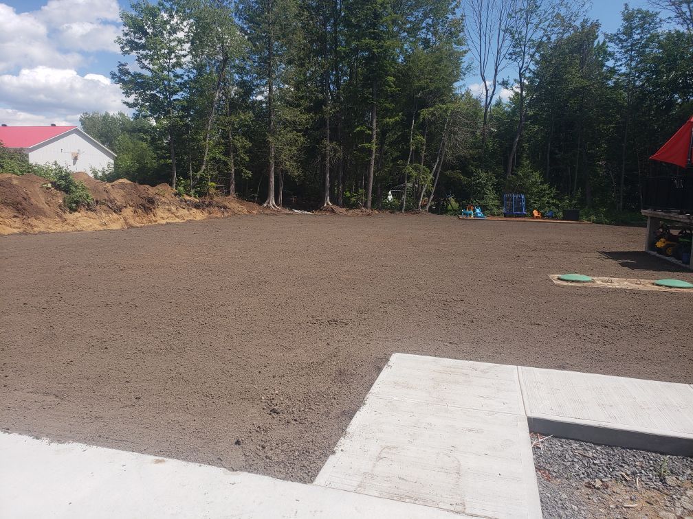 Un grand champ de terre avec des arbres en arrière-plan et une maison en arrière-plan.