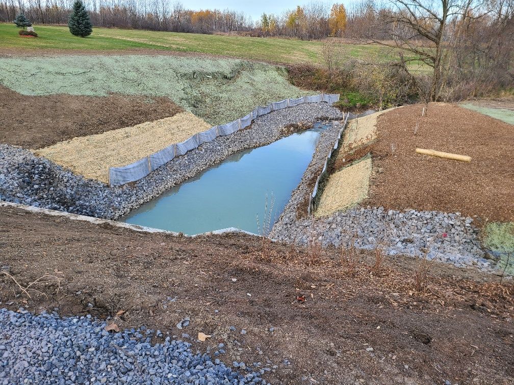 Un petit étang est entouré de rochers et de terre dans un champ.