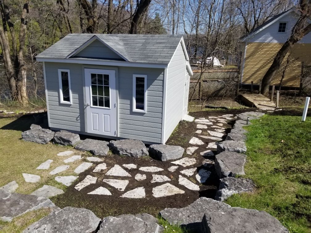 Un petit hangar avec une allée en pierre qui y mène dans une cour arrière.