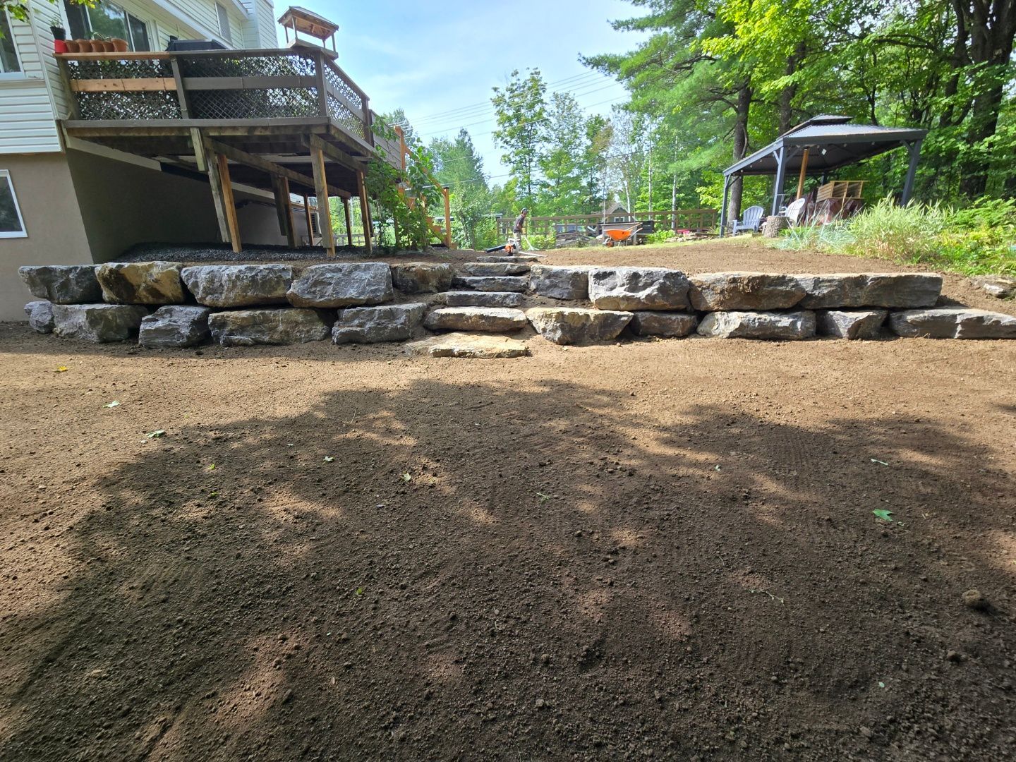 Un mur de pierre est en train d'être construit devant une maison avec une terrasse.