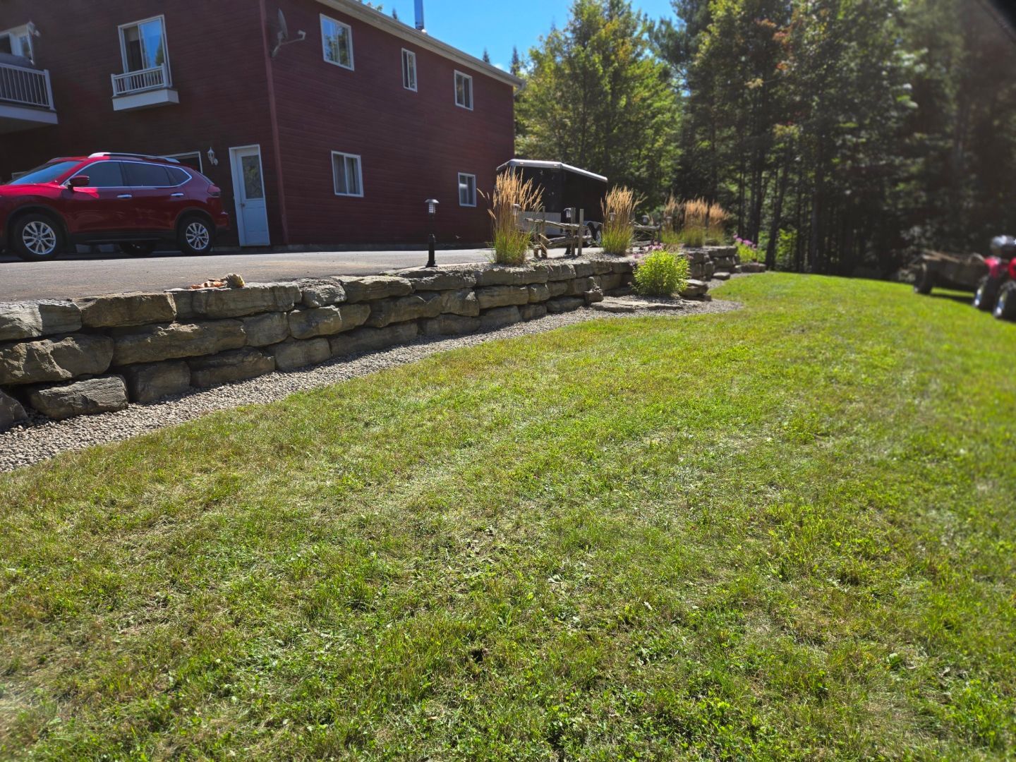 Une voiture rouge est garée devant un bâtiment à côté d'une pelouse verte luxuriante.