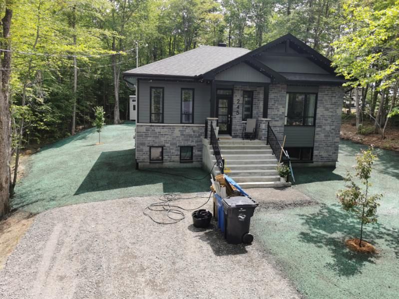 Une maison avec beaucoup d'herbe devant et une poubelle devant.
