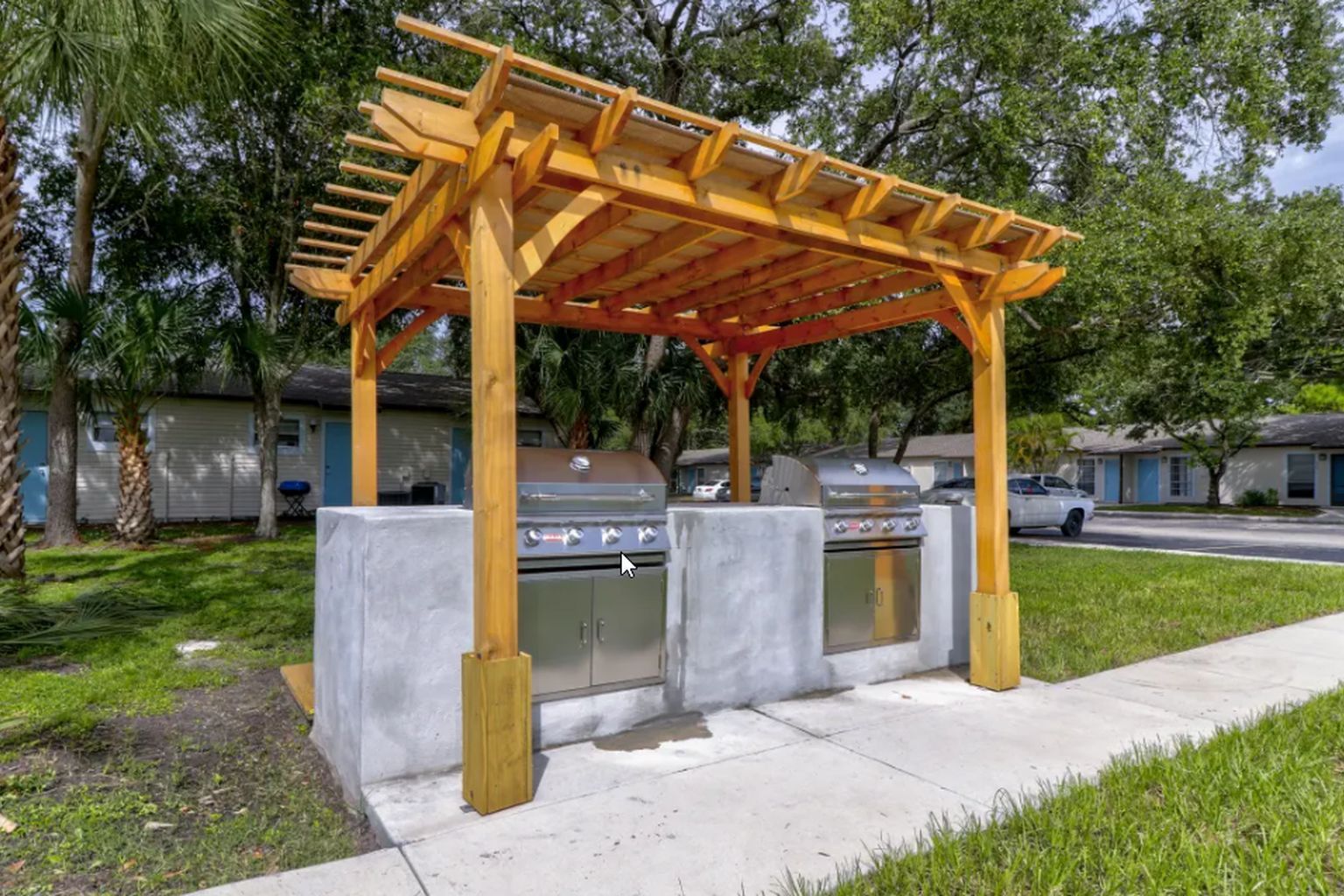 Wooden pergola over concrete grill area with two stainless steel grills.