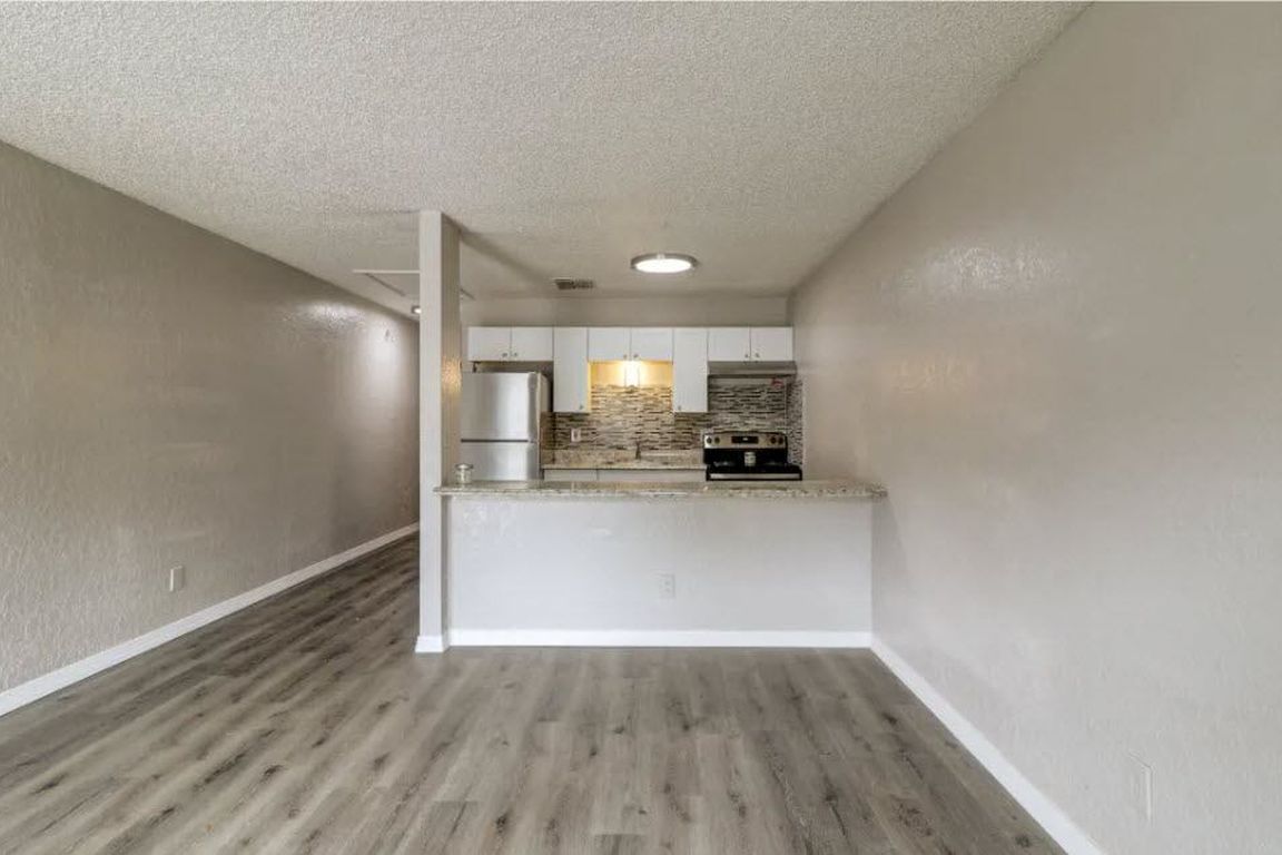 Empty apartment kitchen and living area with gray floors, white walls, and a small breakfast bar.