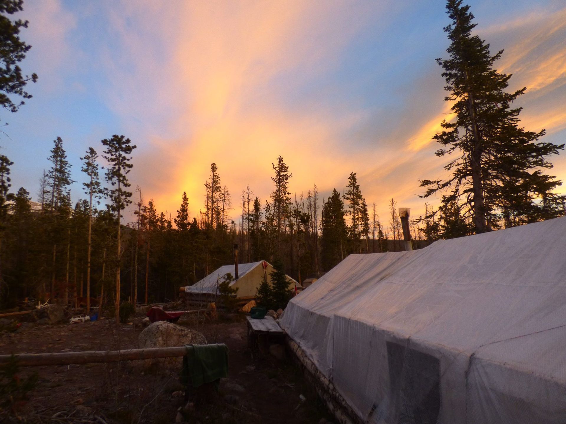 A sunset over a forest with a tent in the foreground