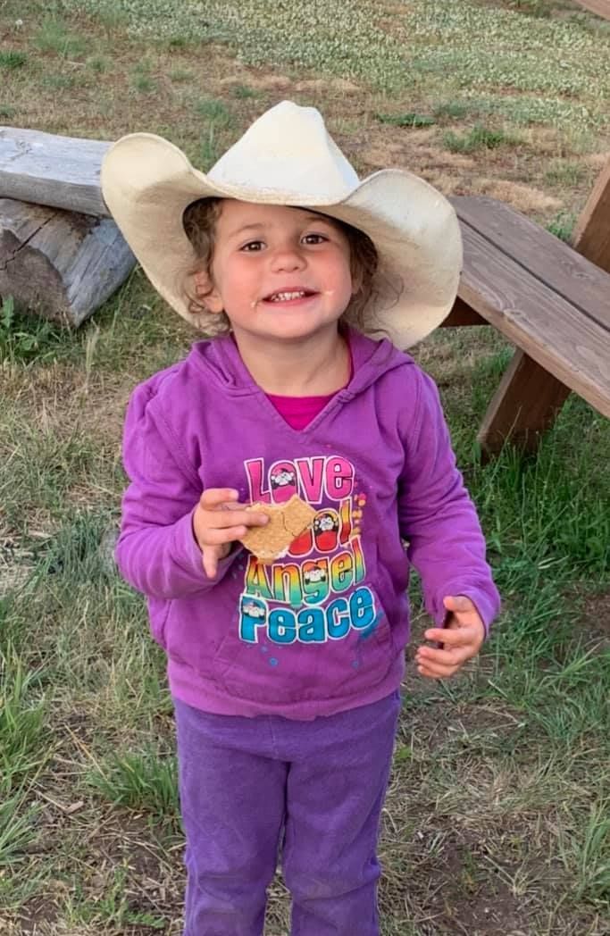 A little girl wearing a cowboy hat and a purple shirt.