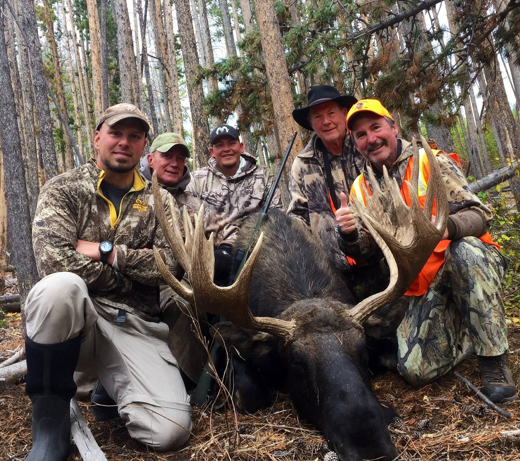 A group of men posing with a moose in the woods