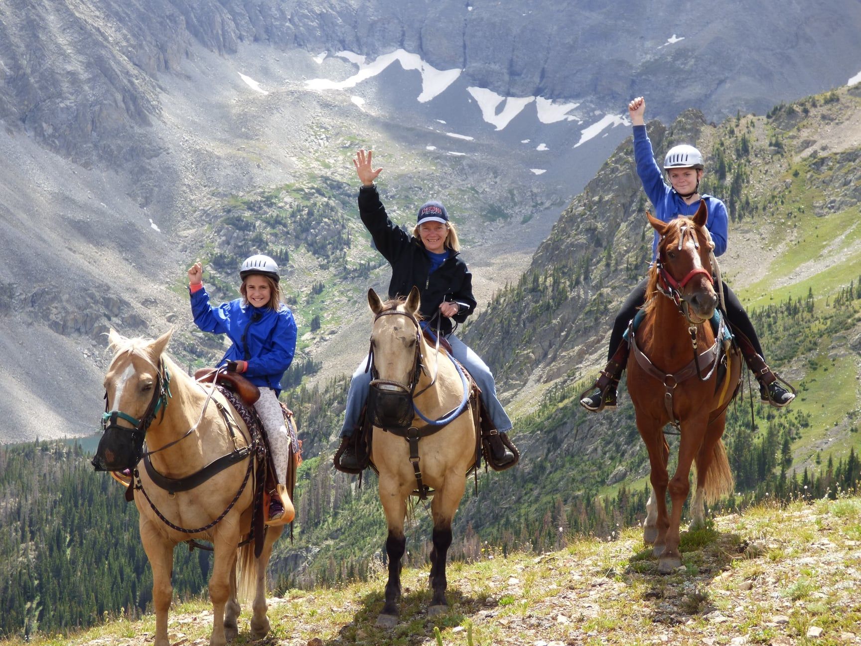 Three people are riding horses on top of a mountain.