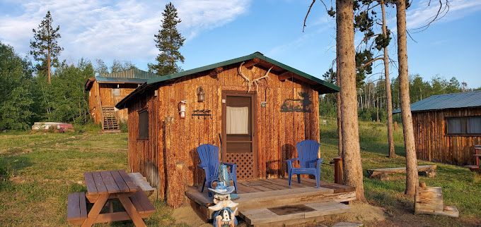 A small wooden cabin with a picnic table and chairs in front of it.
