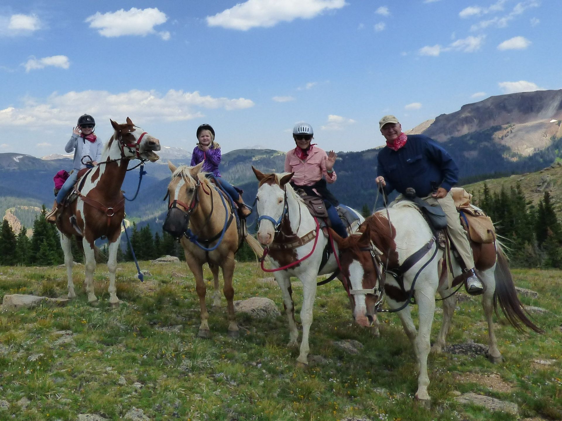 A group of people riding horses in a field with mountains in the background