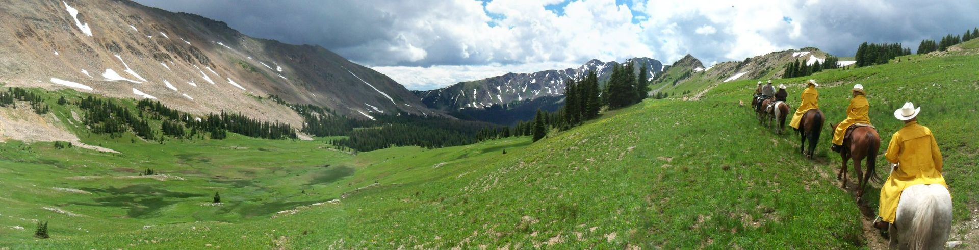 A group of people are riding horses through a grassy field.