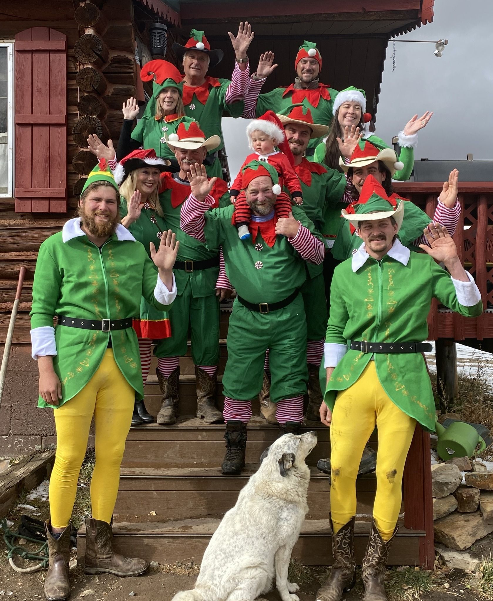 A group of people dressed as elves are posing for a picture with a dog.