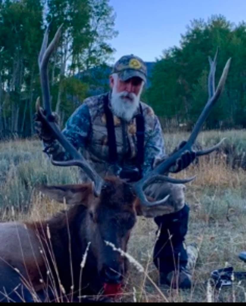 A man with a beard is kneeling next to a deer in a field.