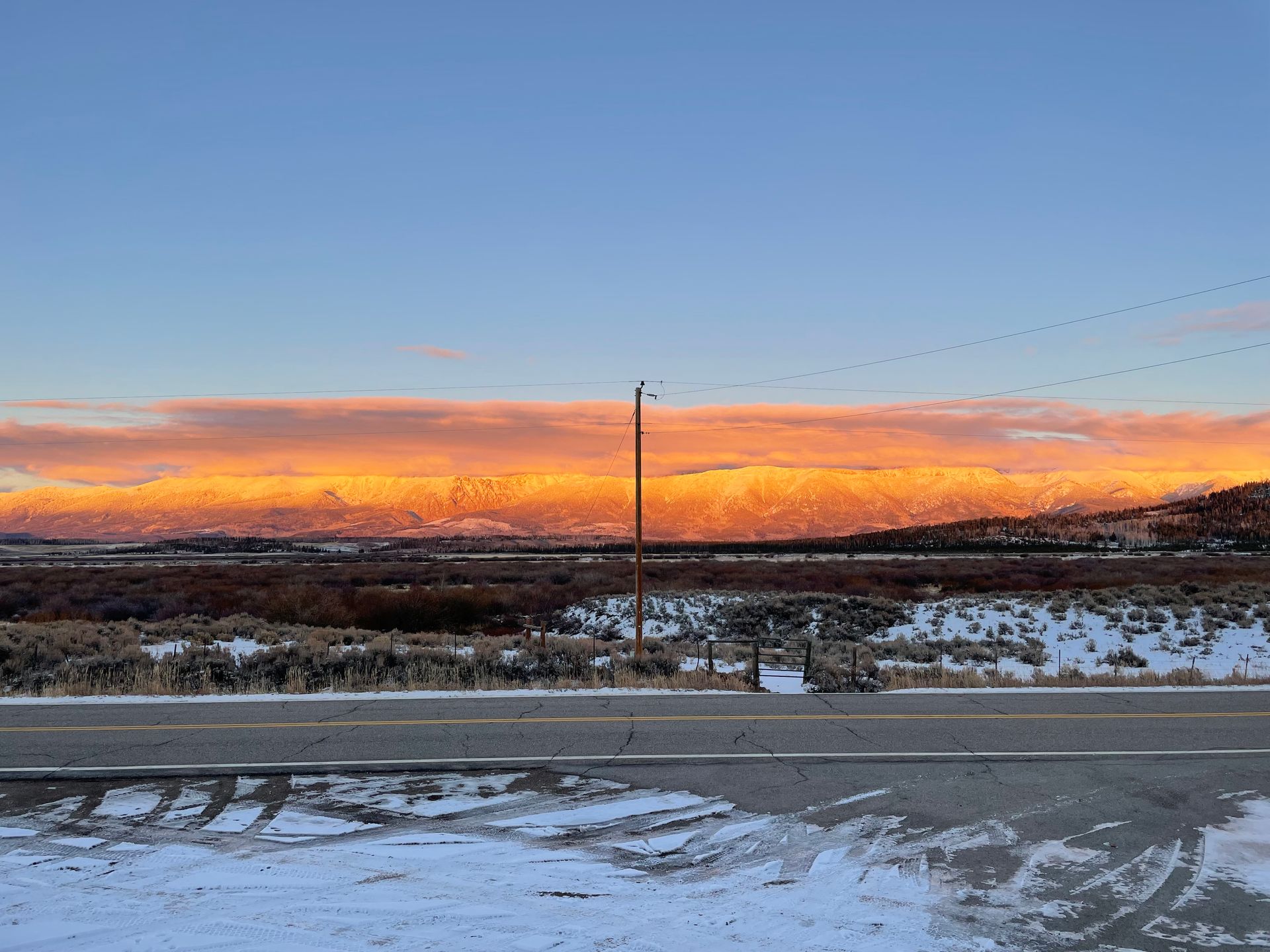 A sunset over a snowy field with a road in the foreground.