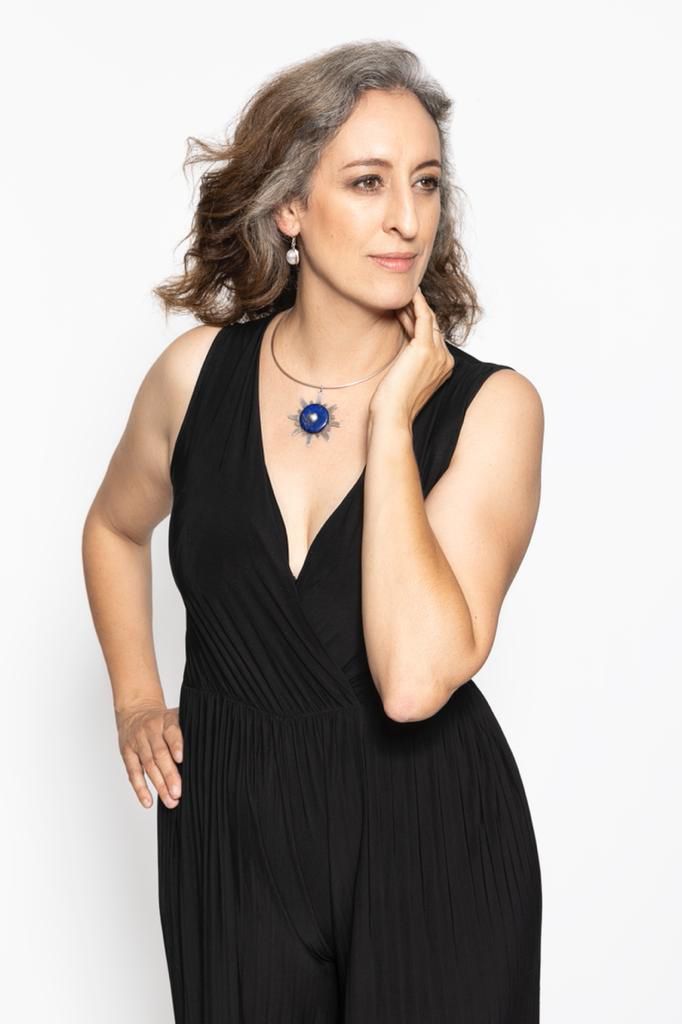 The woman is wearing a black jumpsuit and a blue necklace.