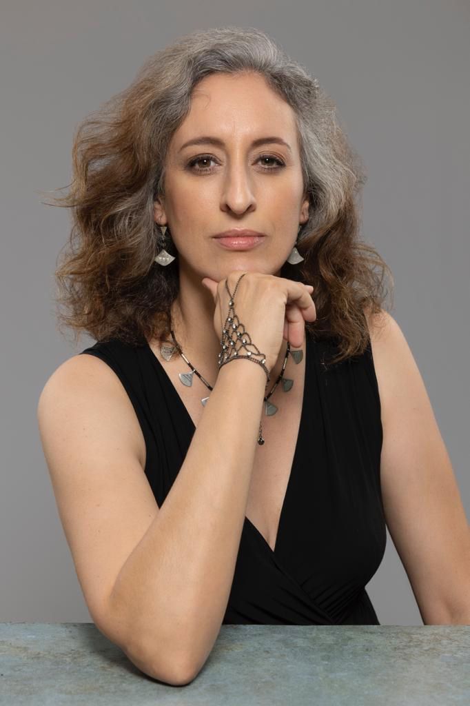 A woman in a black dress is sitting at a table with her hand on her chin.