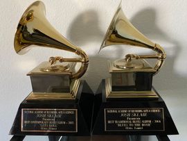 Two gold Grammy trophies on black bases against a white wall.