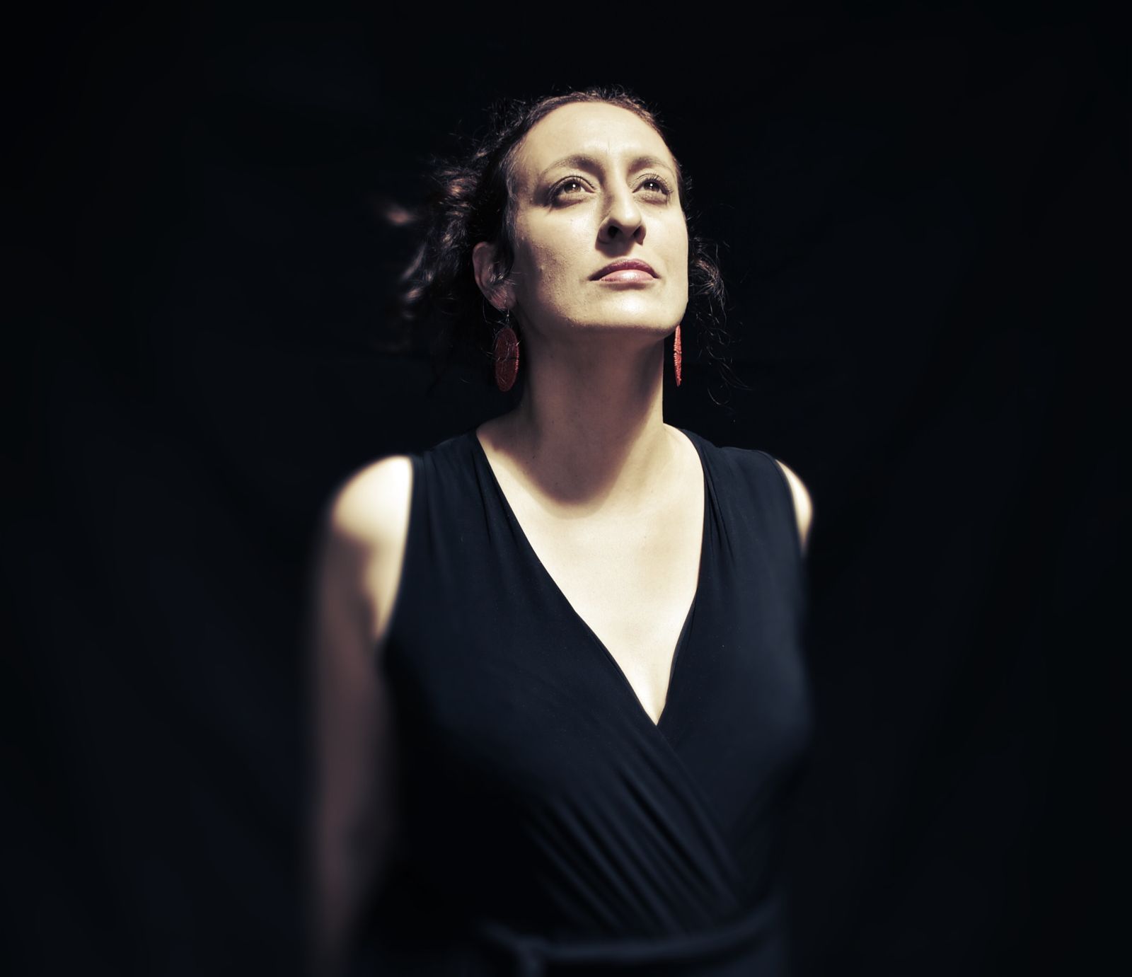 Woman in black dress looking upward with dark background.