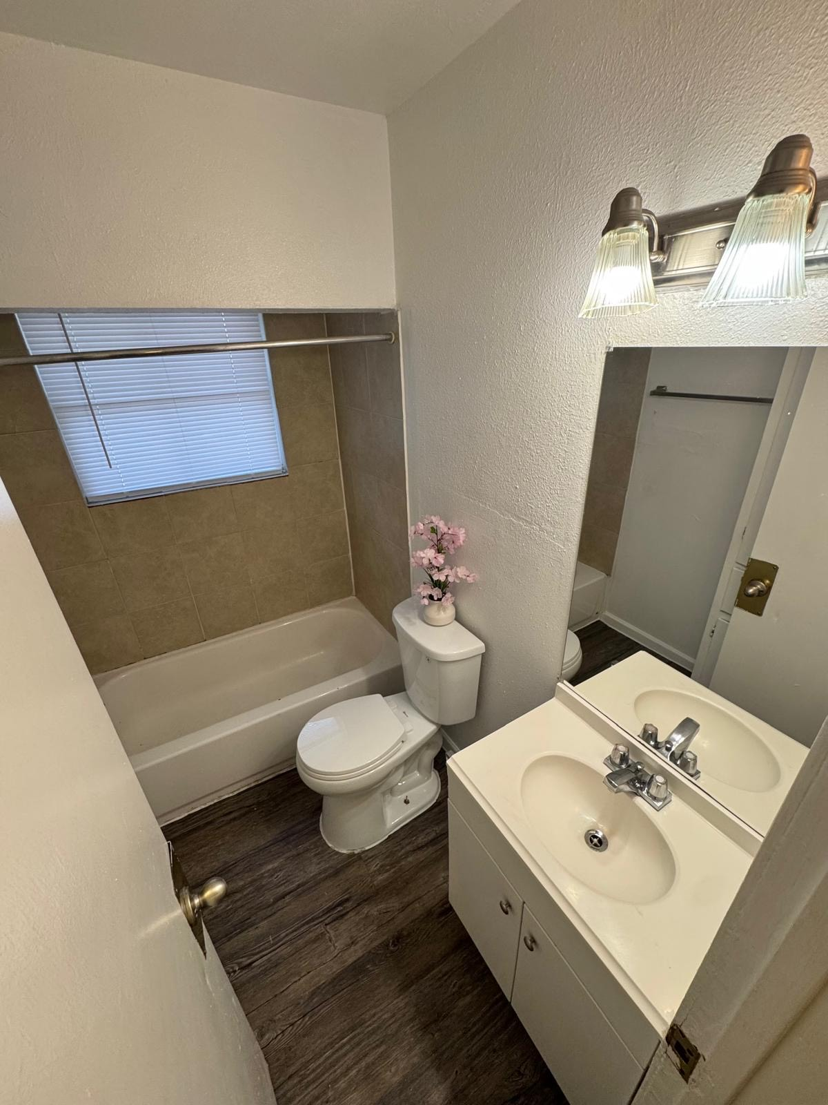Small bathroom with a white toilet, sink, and bathtub. Brown flooring and tan wall tile are visible.
