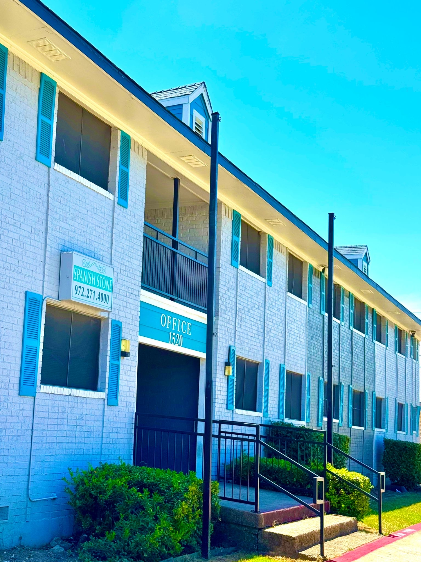 Apartment building with blue shutters and accents, a light blue brick exterior, and a bright sky.