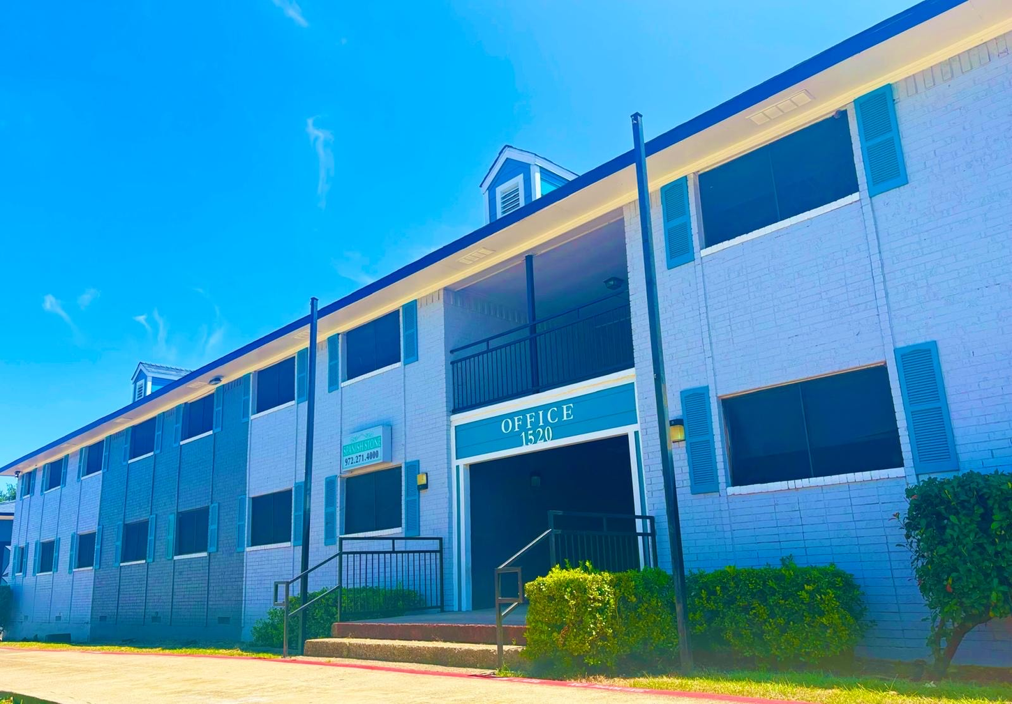 Apartment building exterior on a sunny day. Blue and gray building with blue shutters and a central entrance.