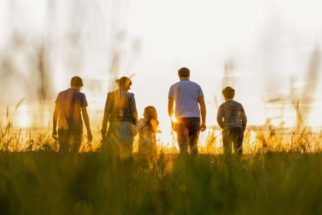 A family is walking through a field at sunset.