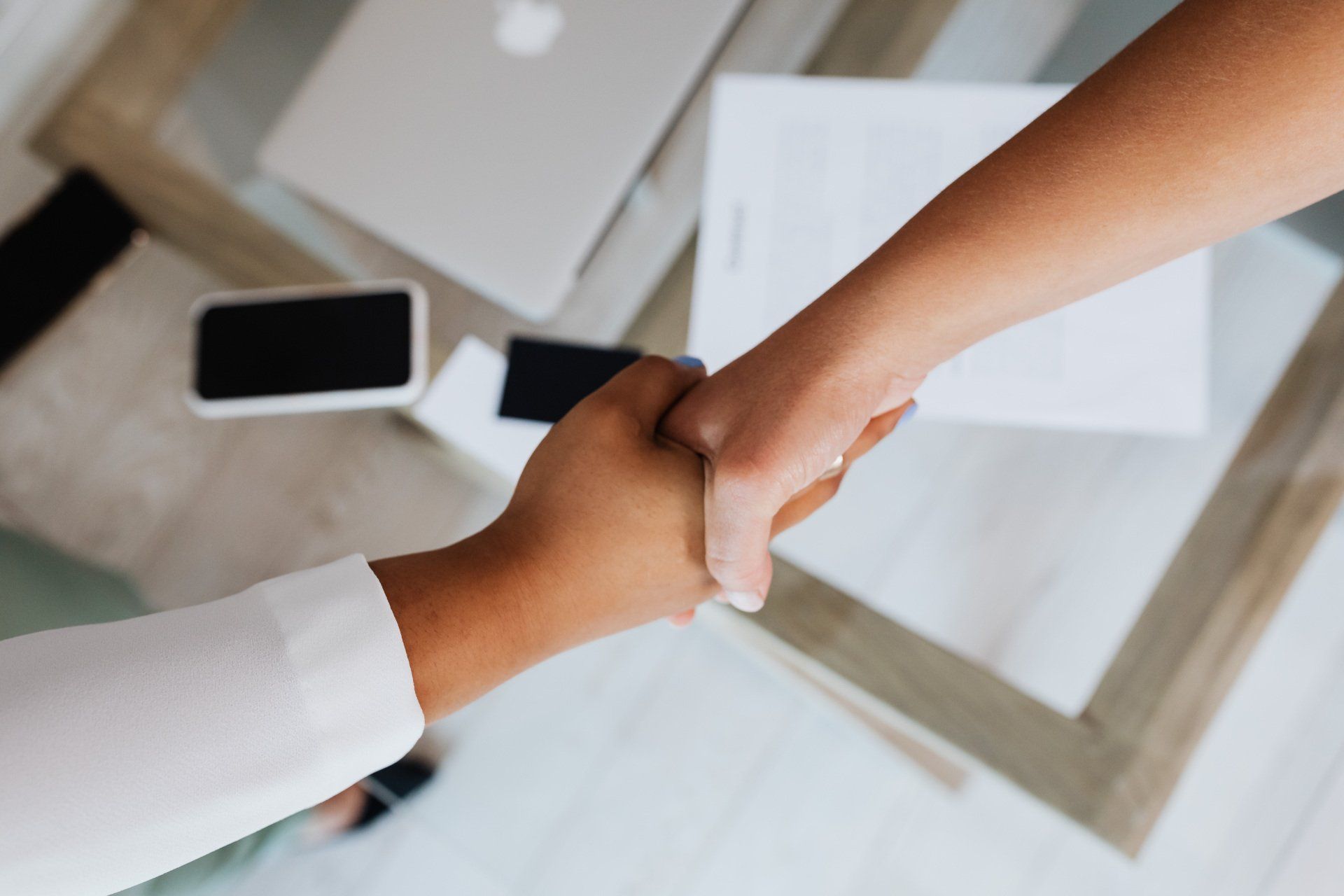 Two people are shaking hands in front of a table.