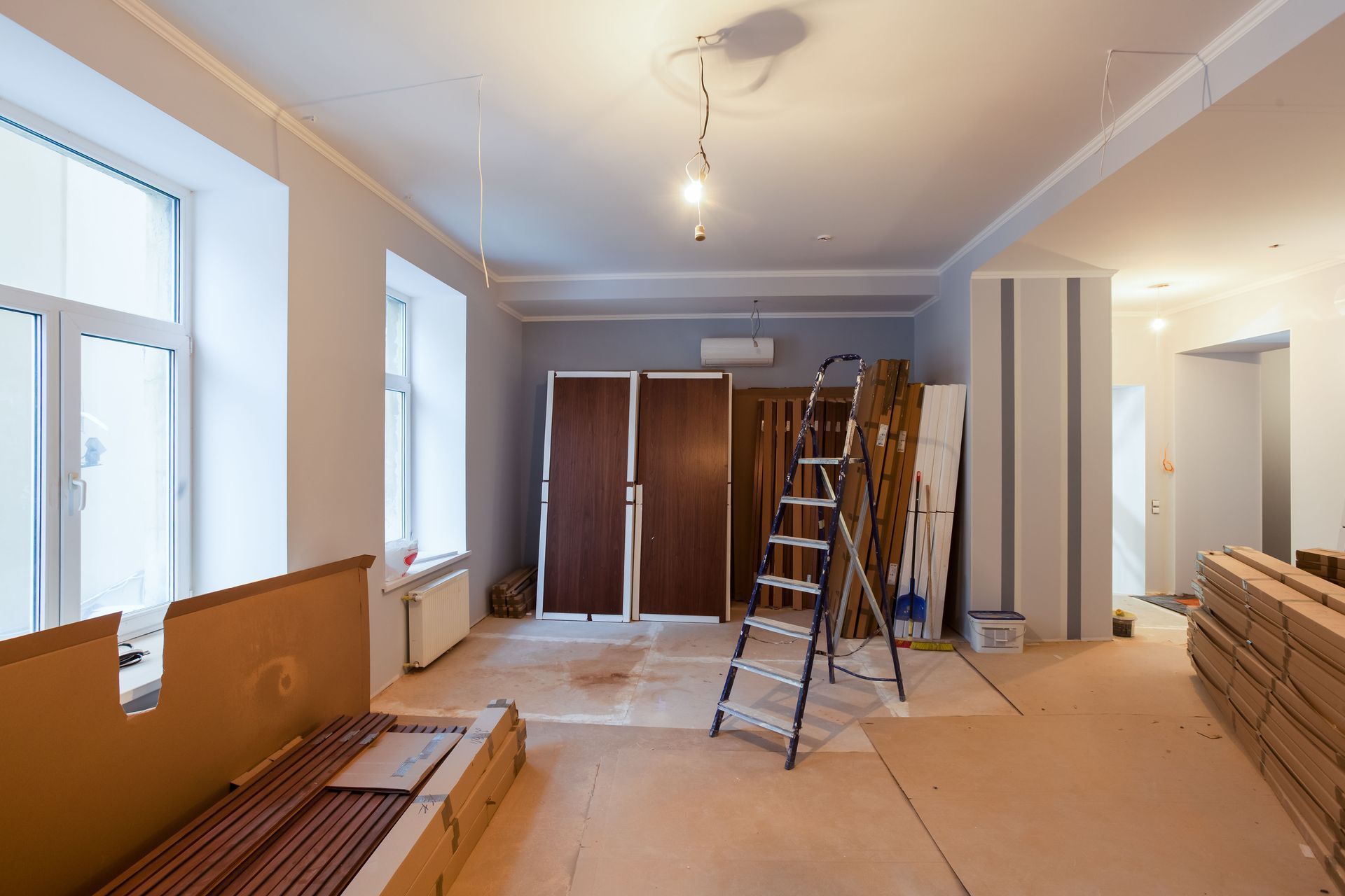 Partially renovated room with ladders, stacked materials, and unfinished walls and ceiling