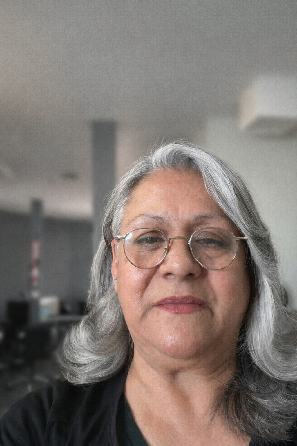 A portrait of a person with shoulder-length, silver hair and thin-rimmed glasses looking directly at the camera.