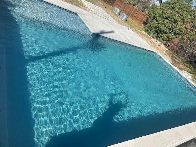 A large swimming pool with a fence around it and trees in the background.