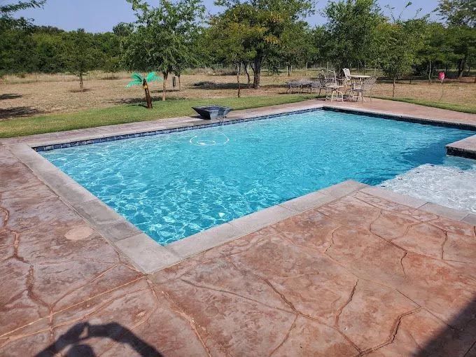 A large swimming pool is surrounded by trees and a patio.
